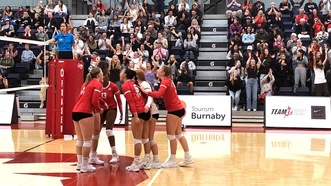 Photo of the volleyball team gathered in a huddle congratulating each other on the court.