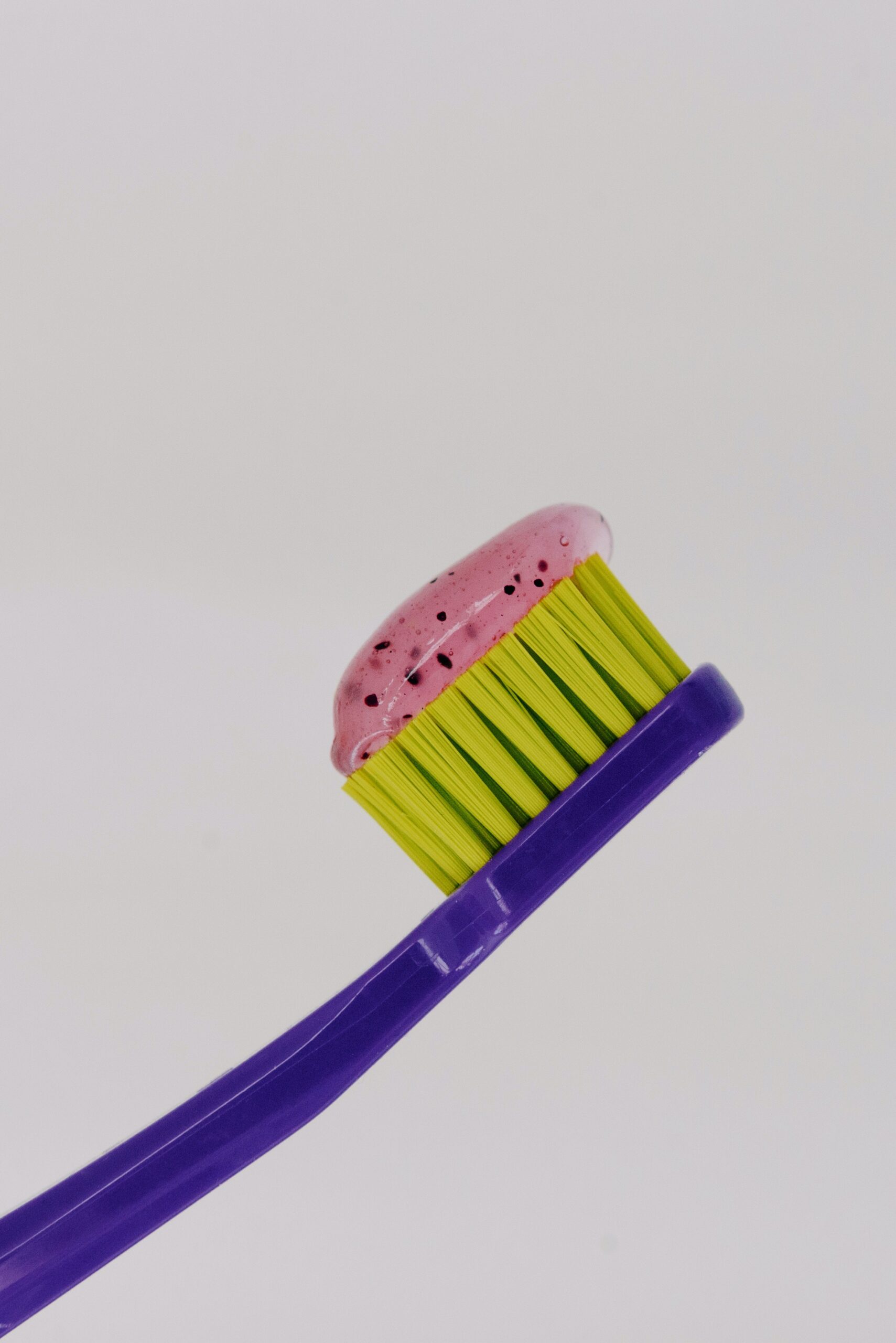 Purple toothbrush with yellow bristles and pink toothpaste on it.