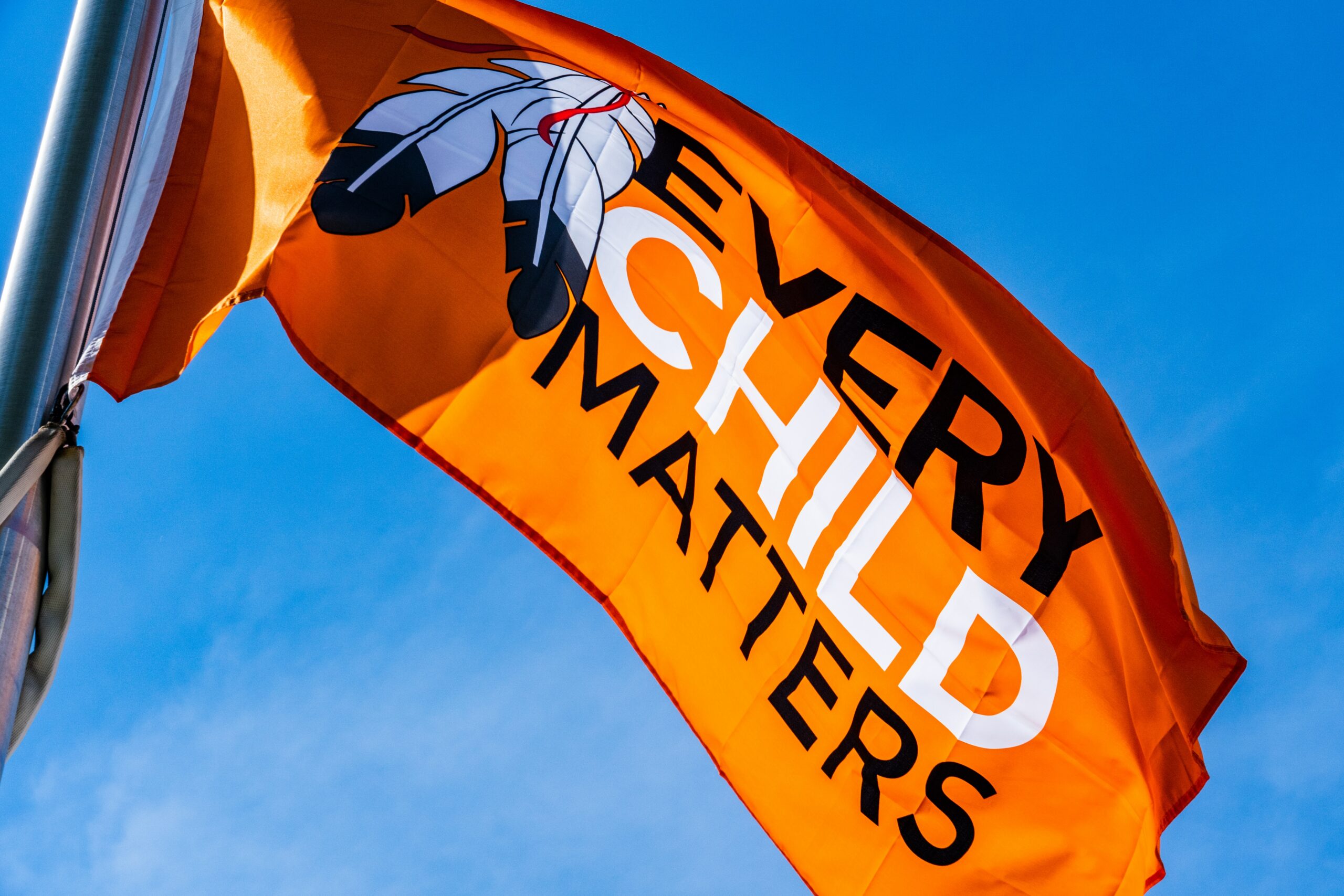 This is an image of an orange, “every child matters” flag. The flag is being blown in the wind so the text is visible.