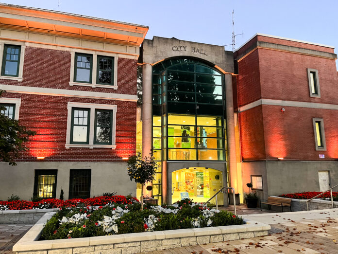 This is a photo of the Port Coquitlam city hall. The building is made of bricks, and the entrance has large windows. There are flowers outside the building in large flowerbeds.