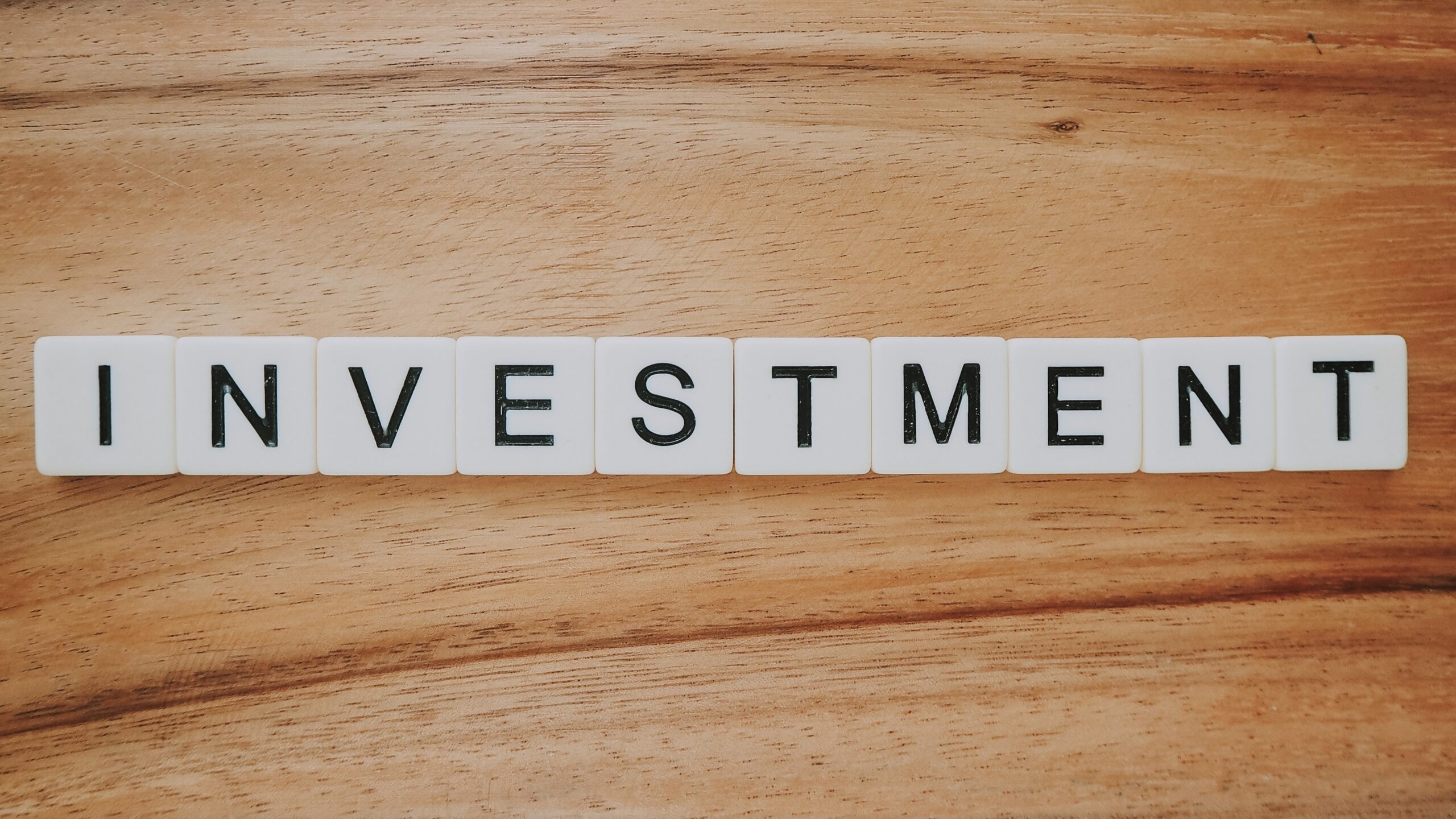 The word investment laid out in Scrabble tiles on a wooden background.