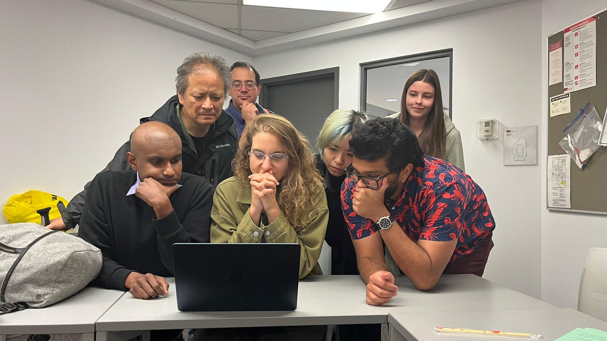 This image is of a small group of TSSU members. They are all leaning over a laptop, and appear deep in thought while looking at the screen.
