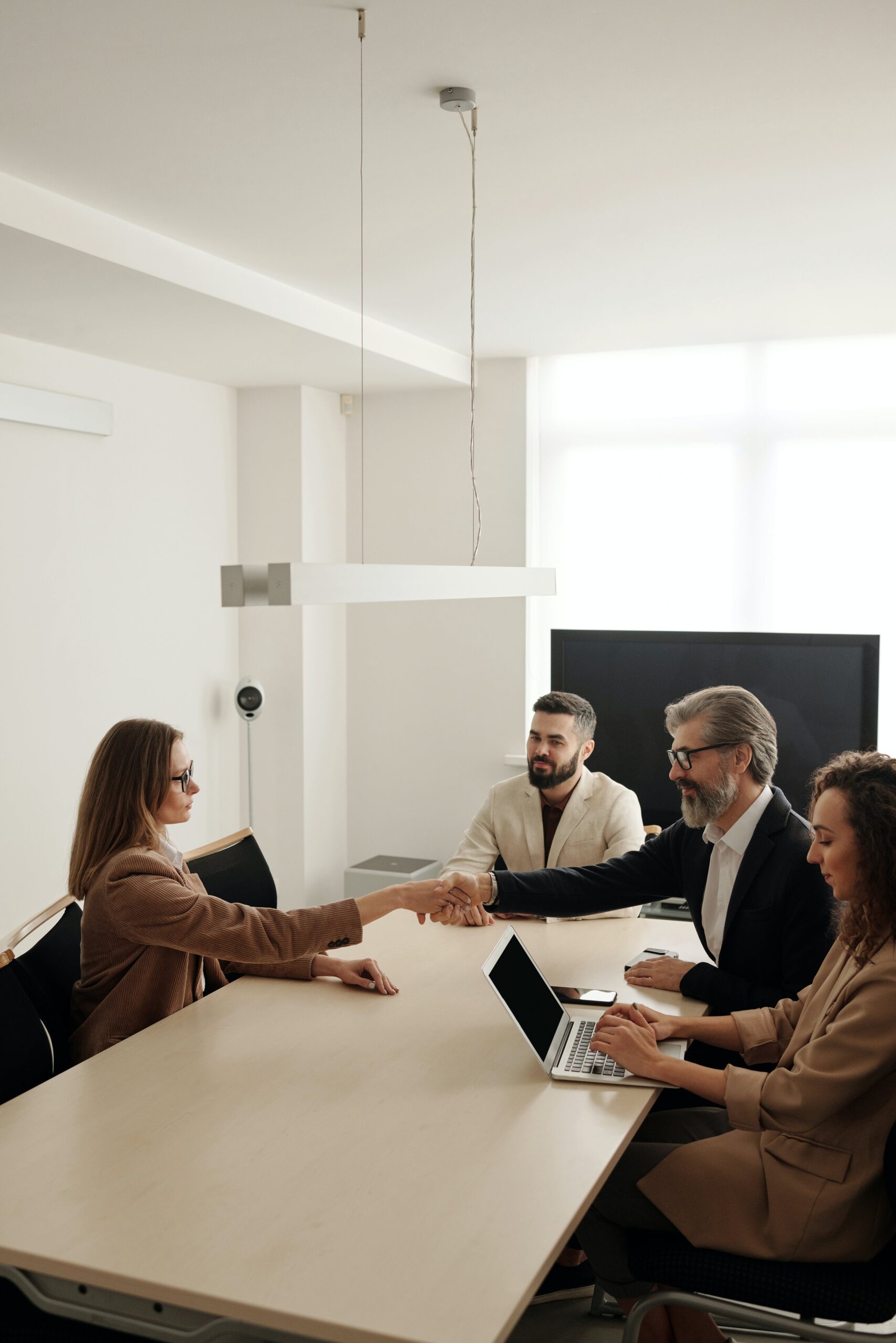 Four business people sitting around a conference table. Two of them are shaking hands.