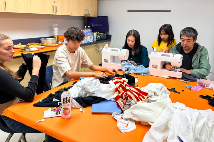 People sitting at a table cutting fabric in front of sewing machines.