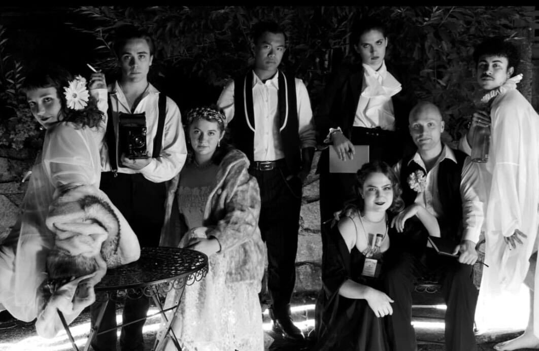 A black and white photo of eight people wearing 1920’s style party wear looking at the camera.