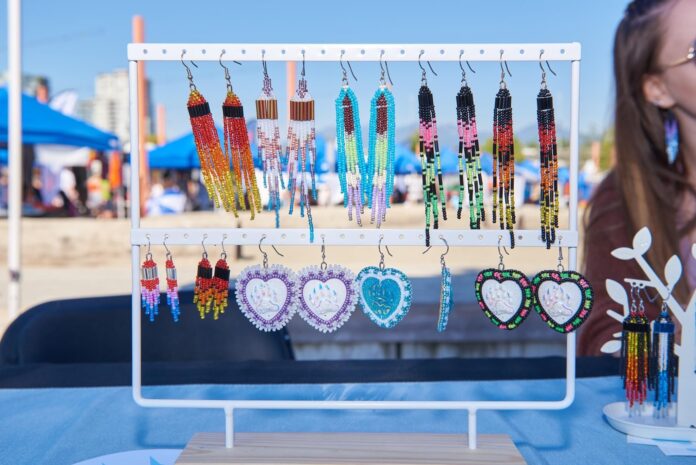 Various beaded fringe earrings of different patterns and colours hang on display at an outdoor vendor market.