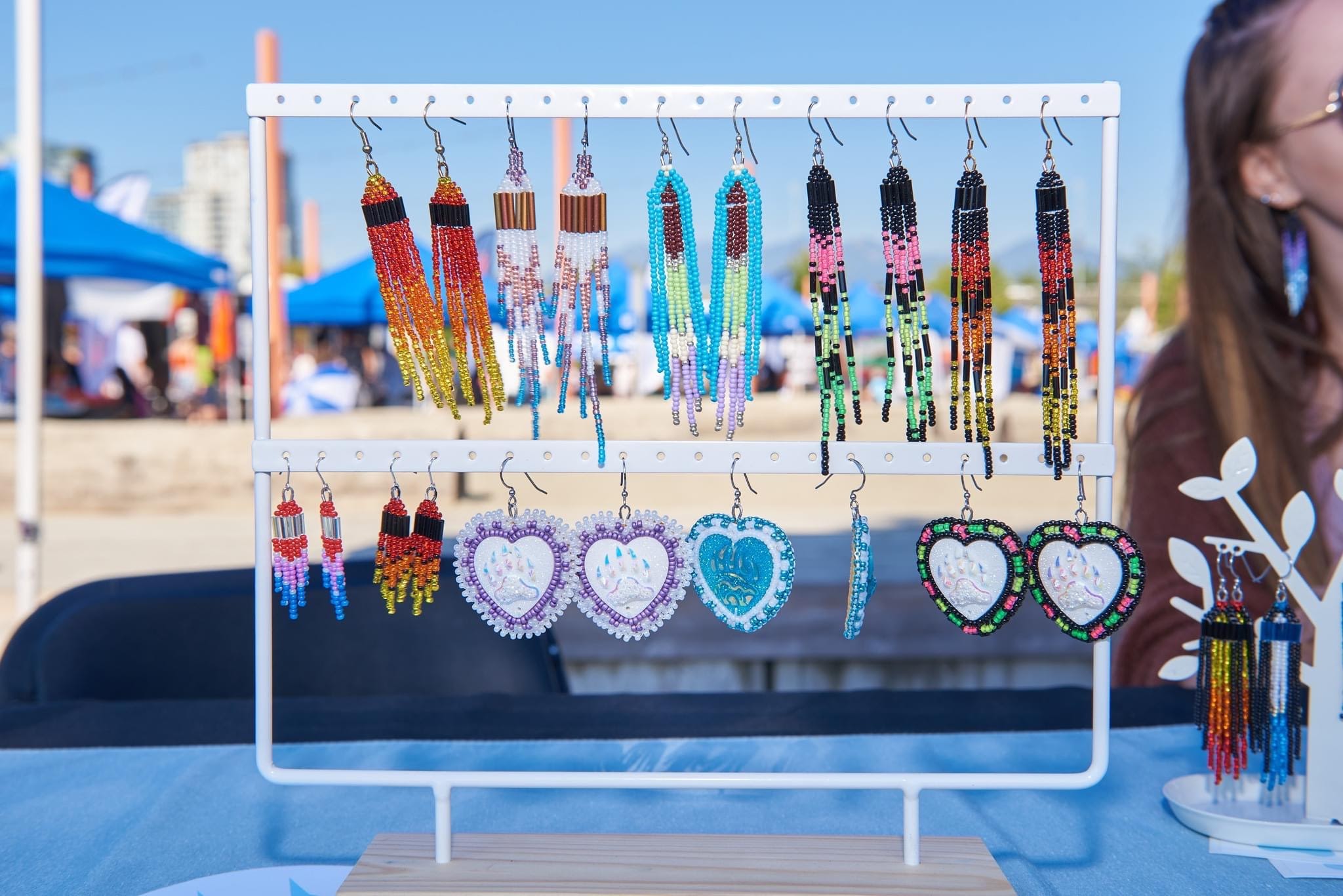 Various beaded fringe earrings of different patterns and colours hang on display at an outdoor vendor market.