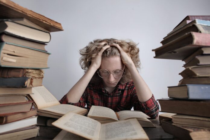 Strike Person wearing a red shirt and glasses surrounded by a large amount of books.