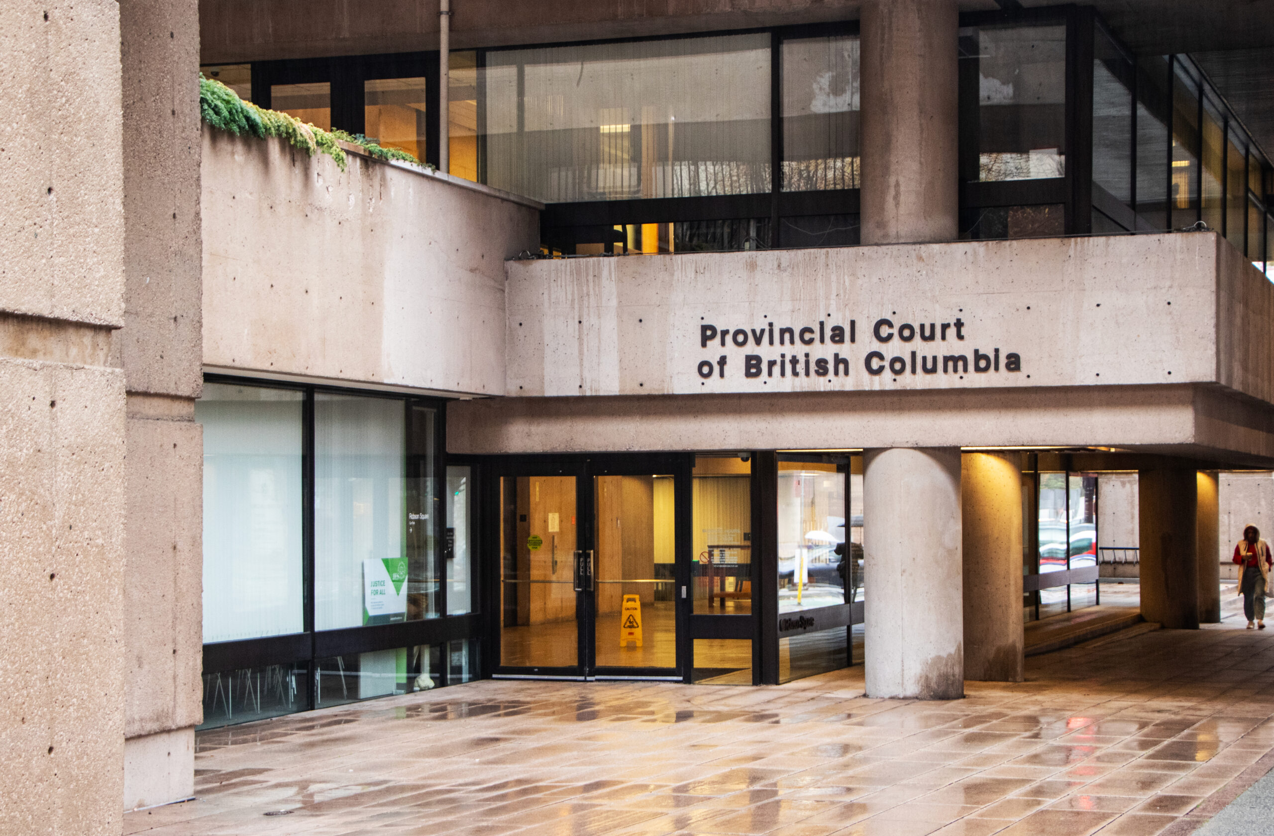 This is a photo of the outside of the Provincial Court of British Columbia. The plain concrete building has a large sign with the name outside.