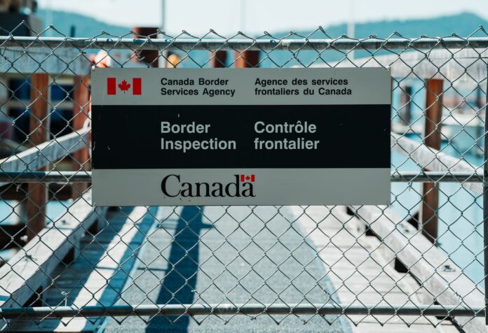 This is a photo of the Canadian border. Specifically, a sign on a metal fence reads, “Canadian Border Inspection.”