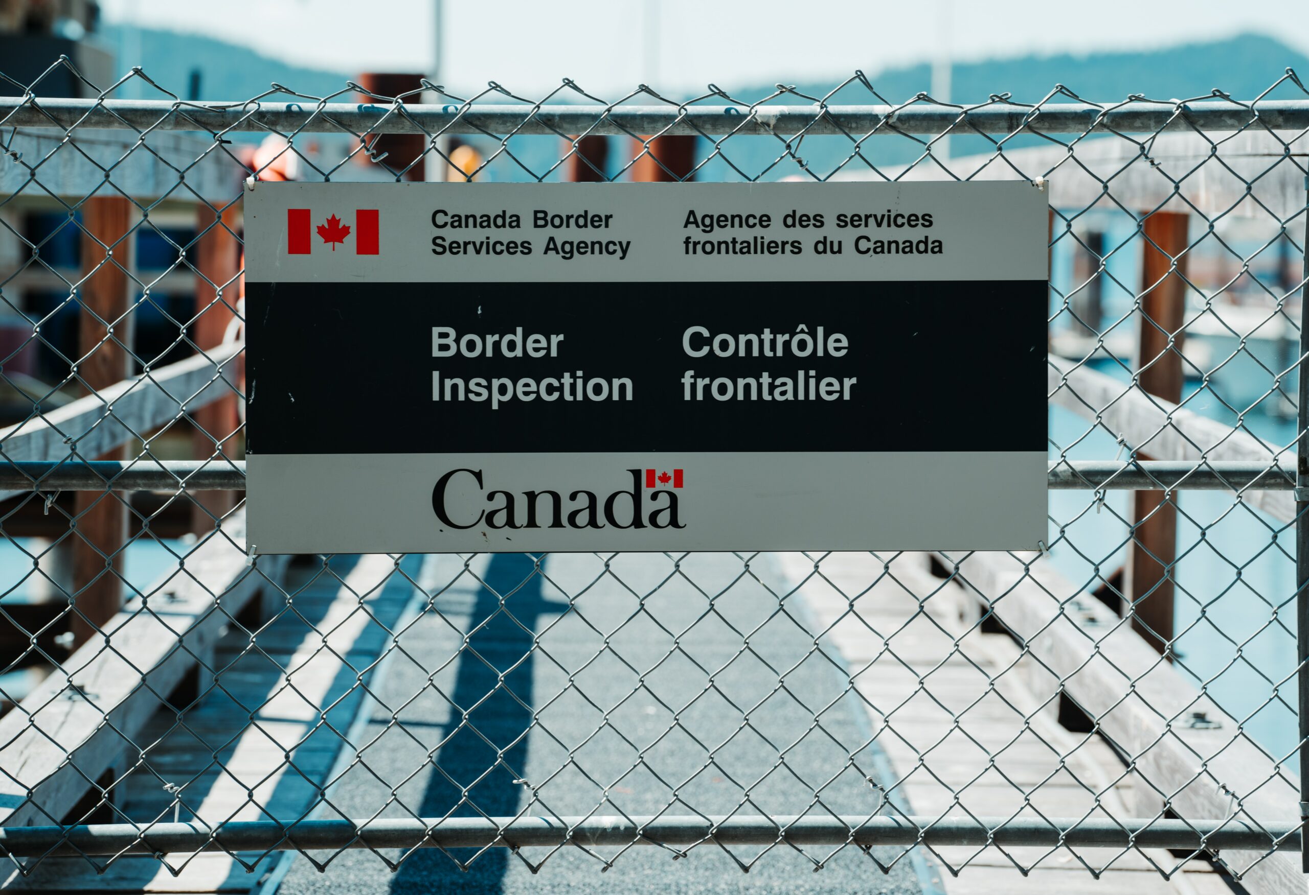 This is a photo of the Canadian border. Specifically, a sign on a metal fence reads, “Canadian Border Inspection.”