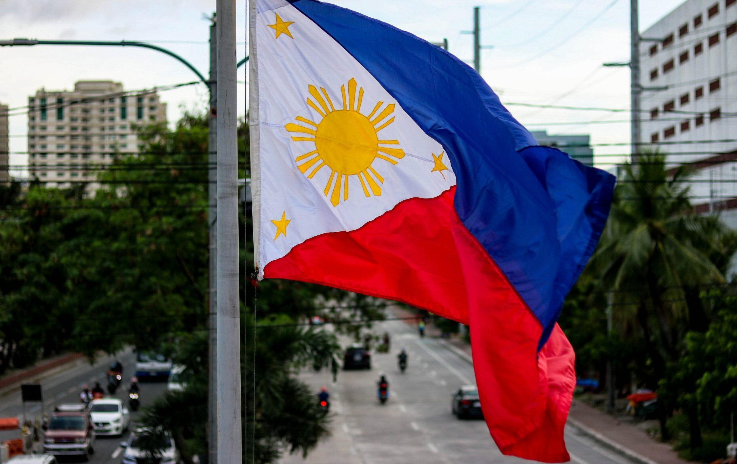 This is an image of the Filipino flag. Their flag is blue and red, with a sun image in the centre. The flag is blowing in the wind on a flagpole outside.