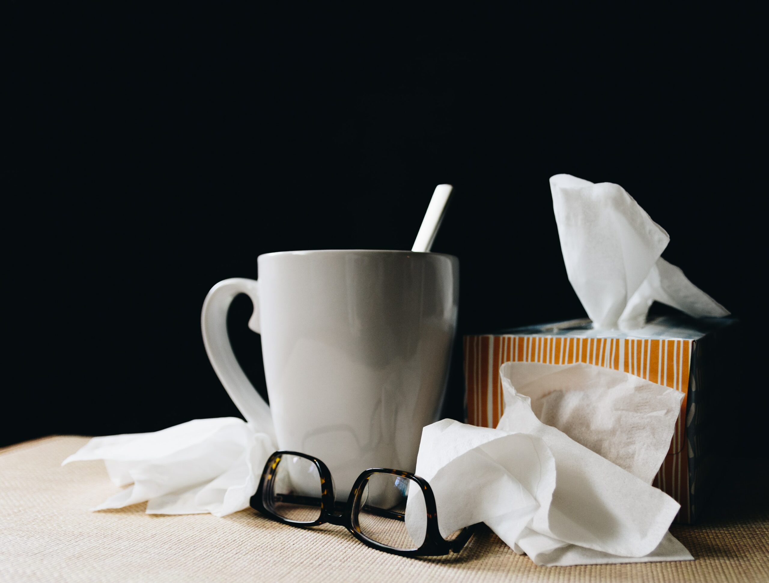 A box of tissues, hot tea, and glasses on a bedside table