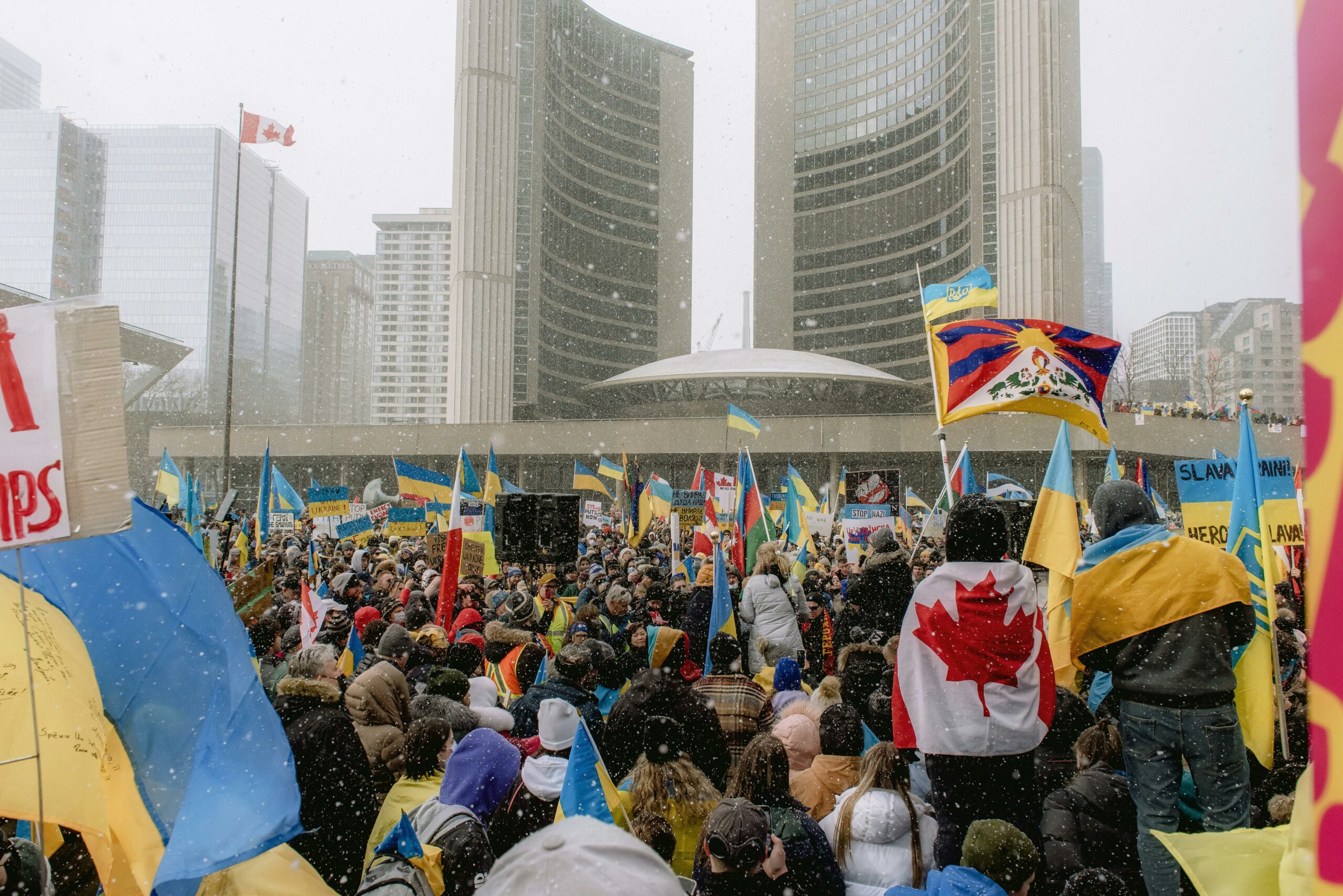 This is a photo of a protest, which happened in Vancouver to support Ukraine. The crowd is varying multiple Canadian flags, and multiple Ukrainian flags.