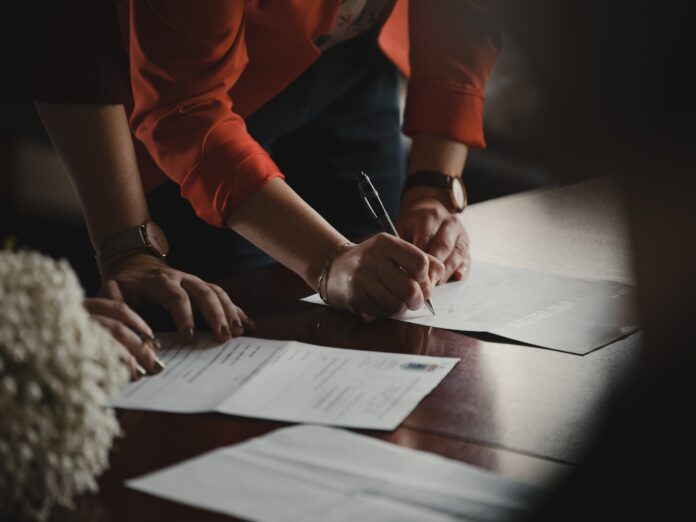 romain-dancre-doplSDELX7E-unsplash This is a photo of a lawyer and client looking at paperwork together. Only their hands are shown, as they write on legal documents.