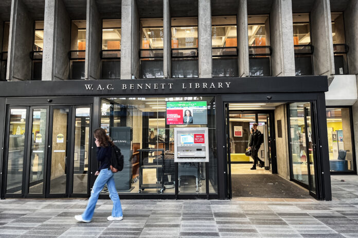 This is a photo of the outside of the Bennett Library at SFU Burnaby Campus. There are students walking past the doors.