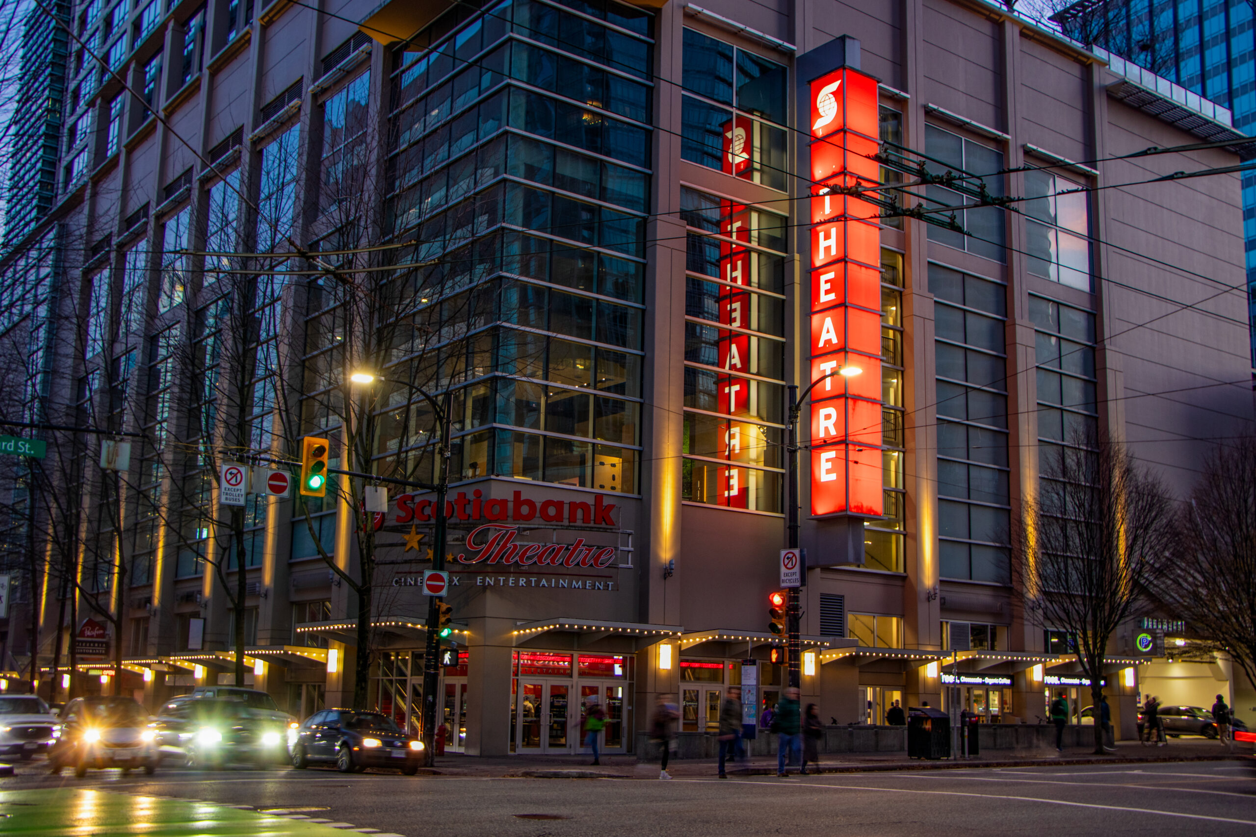 An outdoor sign of scotiabank theatre in front of a busy road on a dim evening.