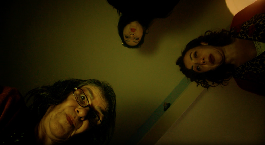 A film still of Hair. A dark, out of focus whimsical shot from below as 3 woman look down at the camera.