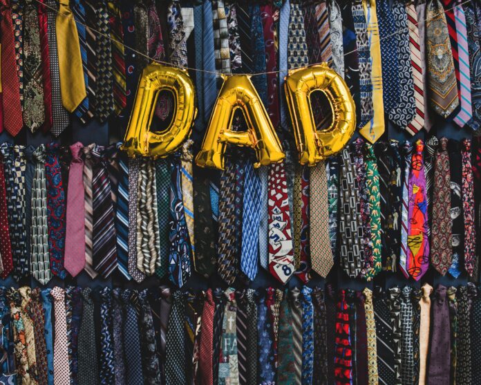 Dad-sona Gold balloons spelling “dad” in front of a wall of ties.