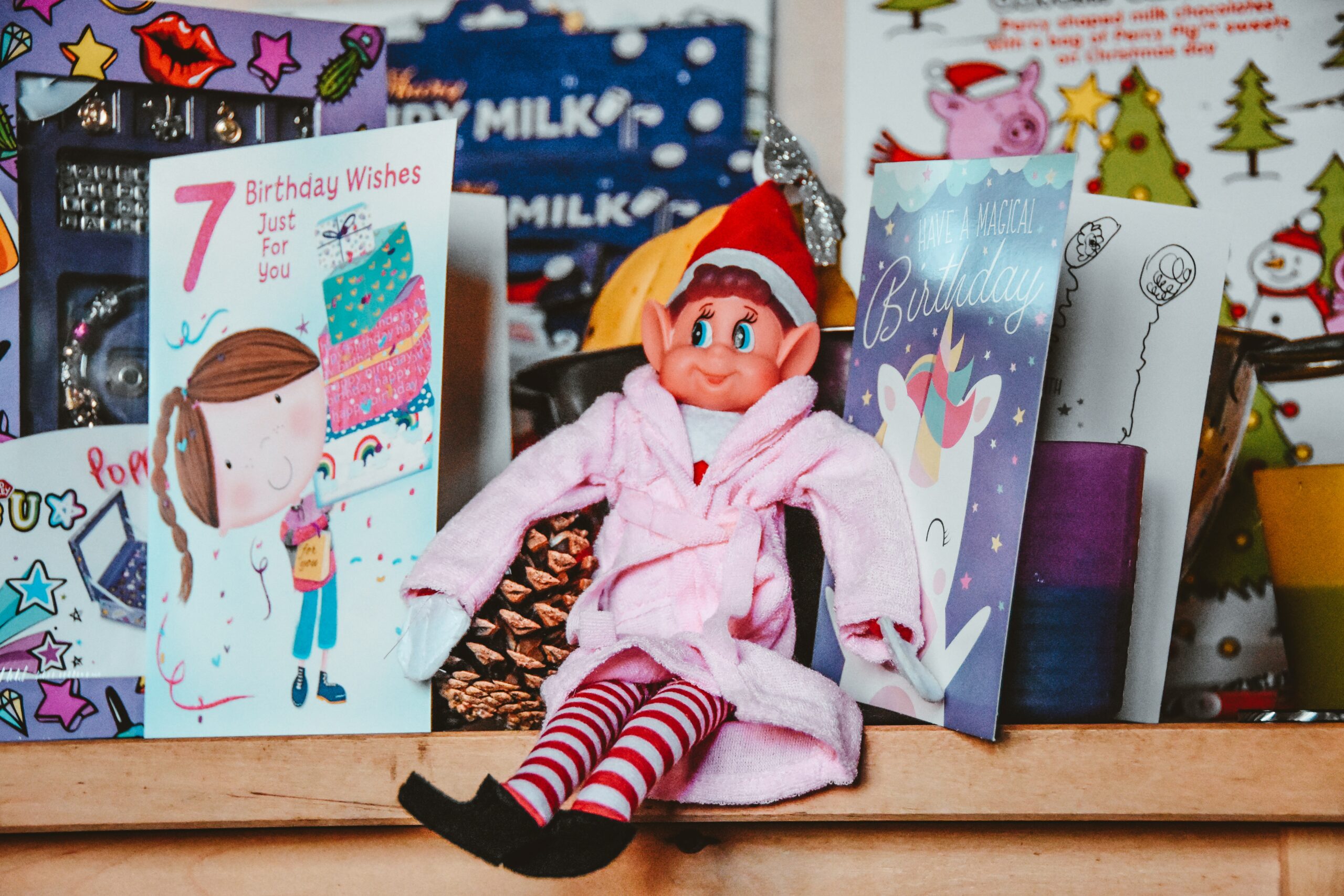 Elf on the Shelf wearing a robe surrounded by birthday cards.