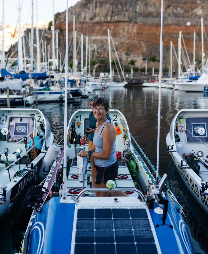 This is a photo of the rowers on their boat in the harbour. The large rowing boat has oars, personal effects, and two rowers standing in the centre.