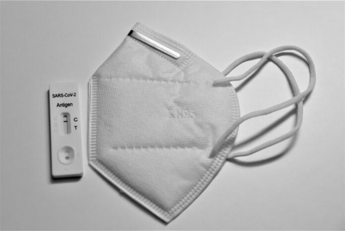 A photo of a COVID-19 antigen test and a KN95 mask.
