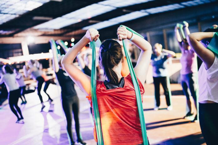 Woman stretching behind her back with a resistance band in a group fitness class setting.