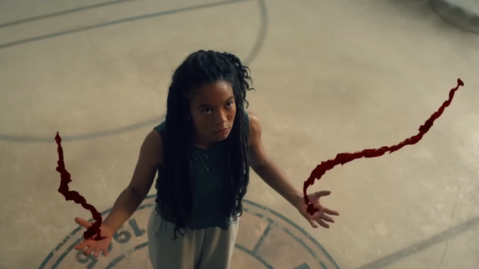 A still from the series Gen V featuring a woman looking up, holding out her hands with blood spurting up into the air.