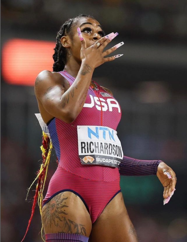 American track runner Sha’Carri Richardson with her hand to her mouth, showcasing her acrylic nails.