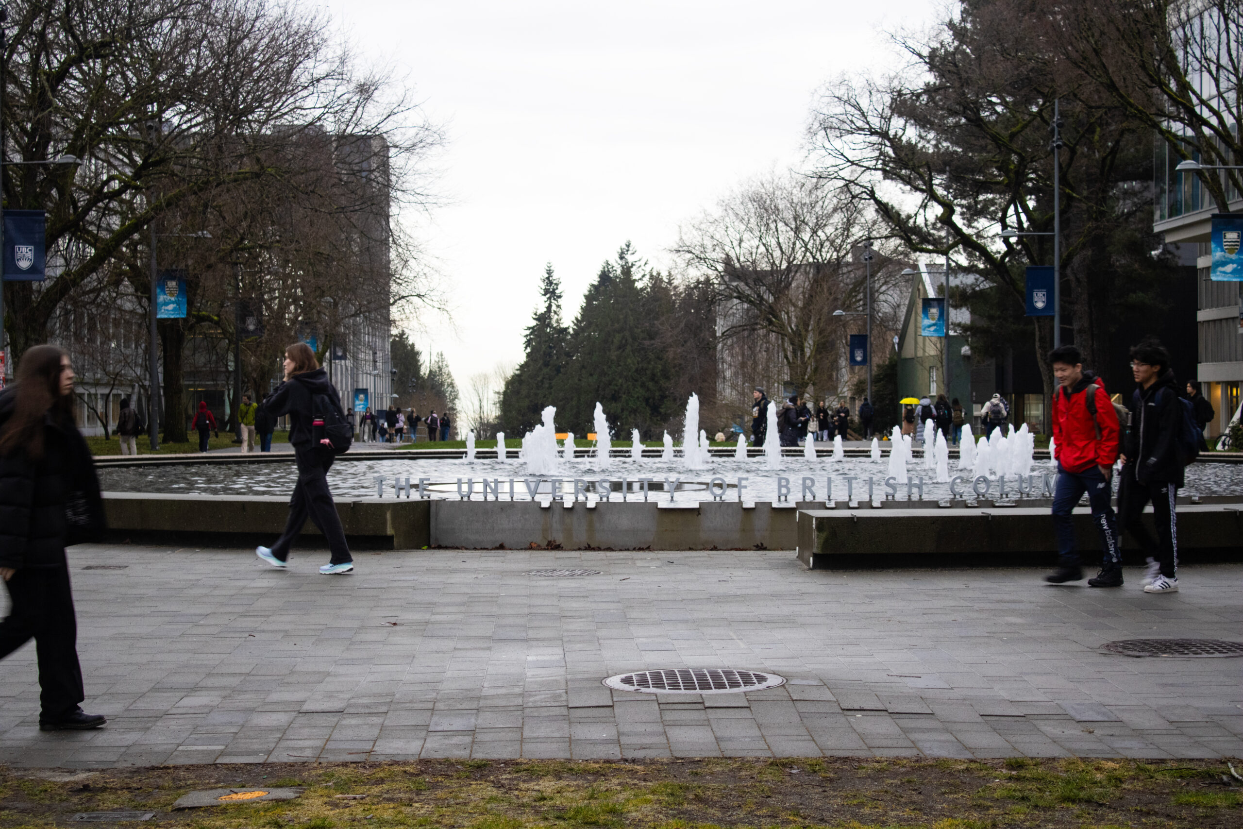 This is a photo of a large water fountain in the middle of a UBC courtyard. The fountain has the words “University of British Columbia” written around the outside. Students are walking around the courtyard.