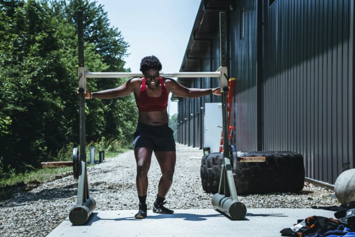 alora-griffiths-2wsKakiqy6I-unsplash Gym goer outside lifting a rack.