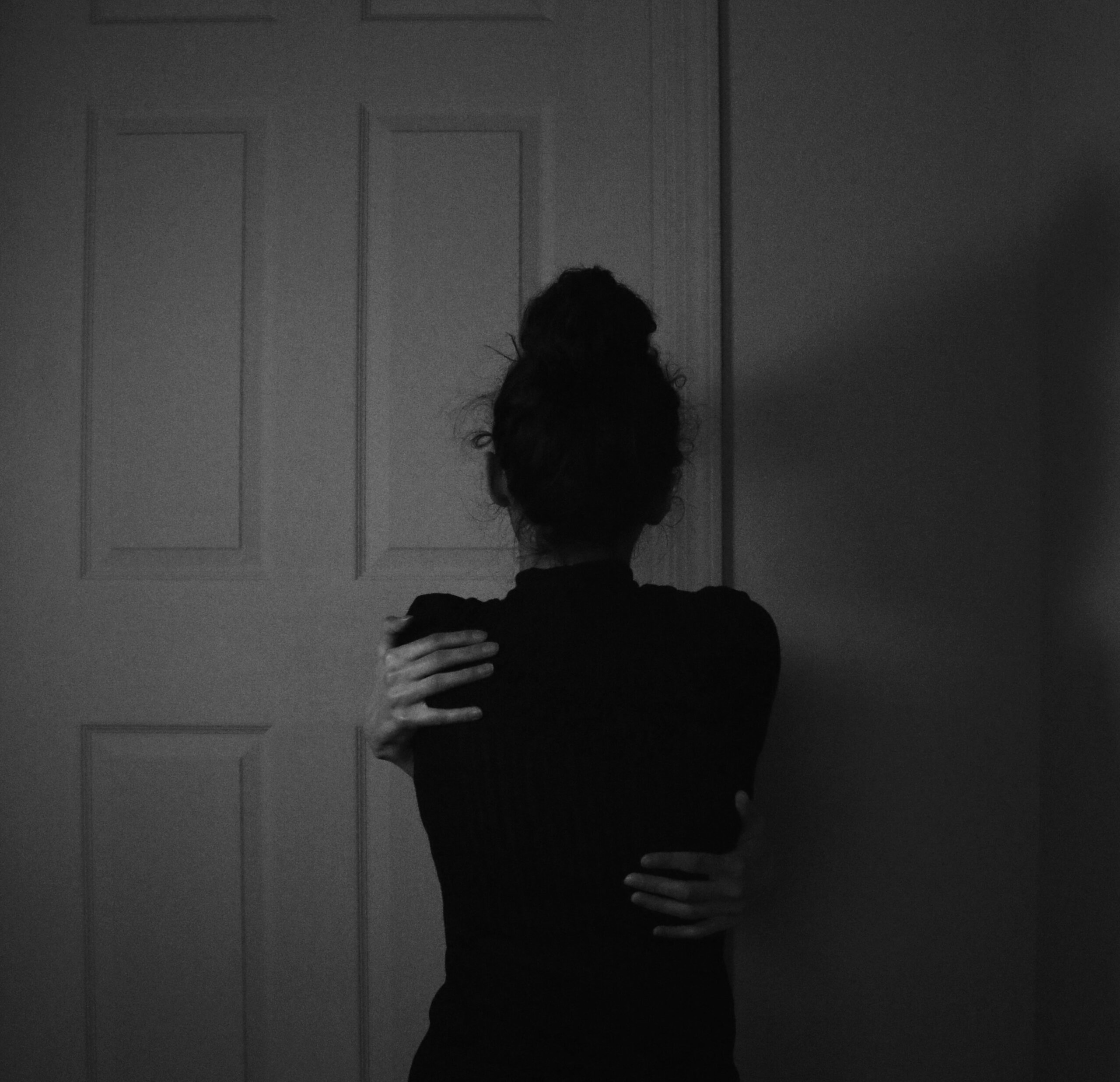 woman in black dress standing near white wooden door with her back facing the camera