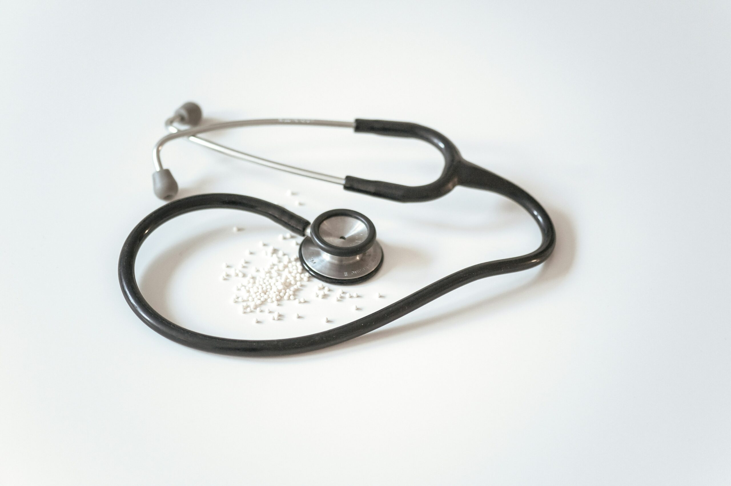 Photo of a black stethoscope surrounded by white pills against a grey background