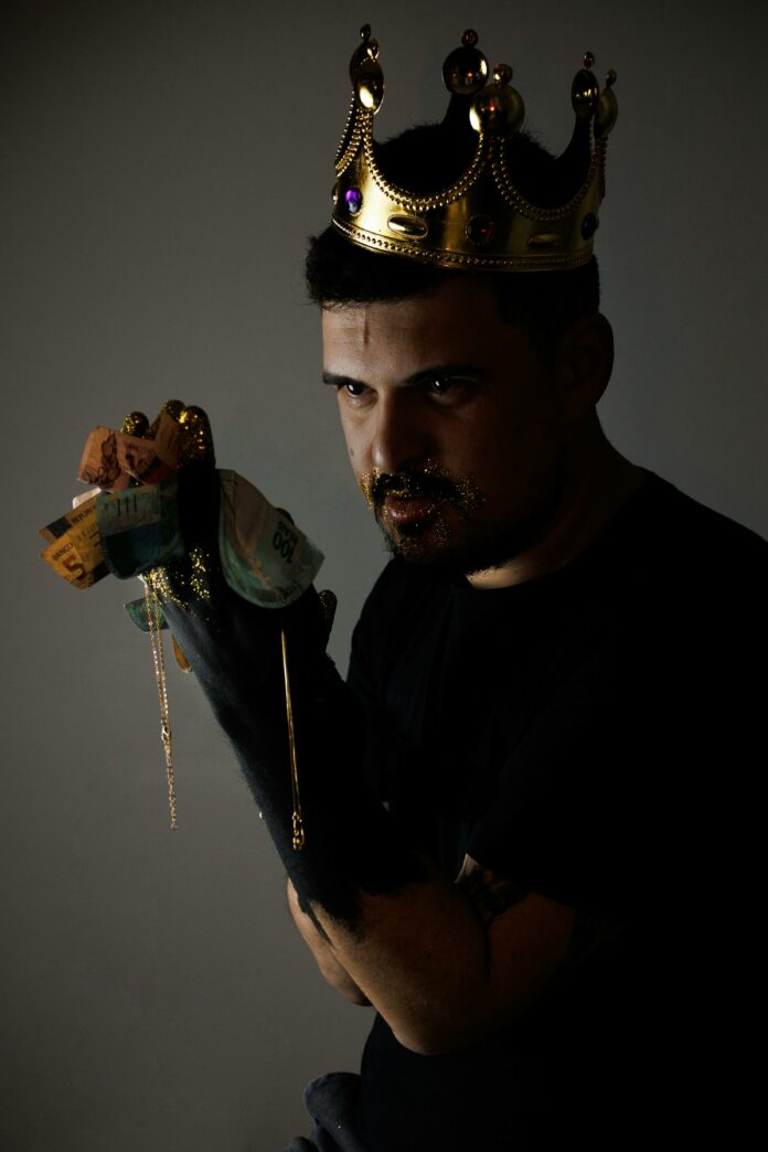 Man wearing a crown and holding banknotes. He has gold glitter in his beard.