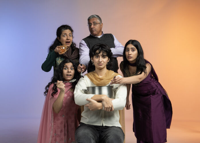 A Pakistani family with quirky expressions surround a young woman holding a pot who looks concerned.