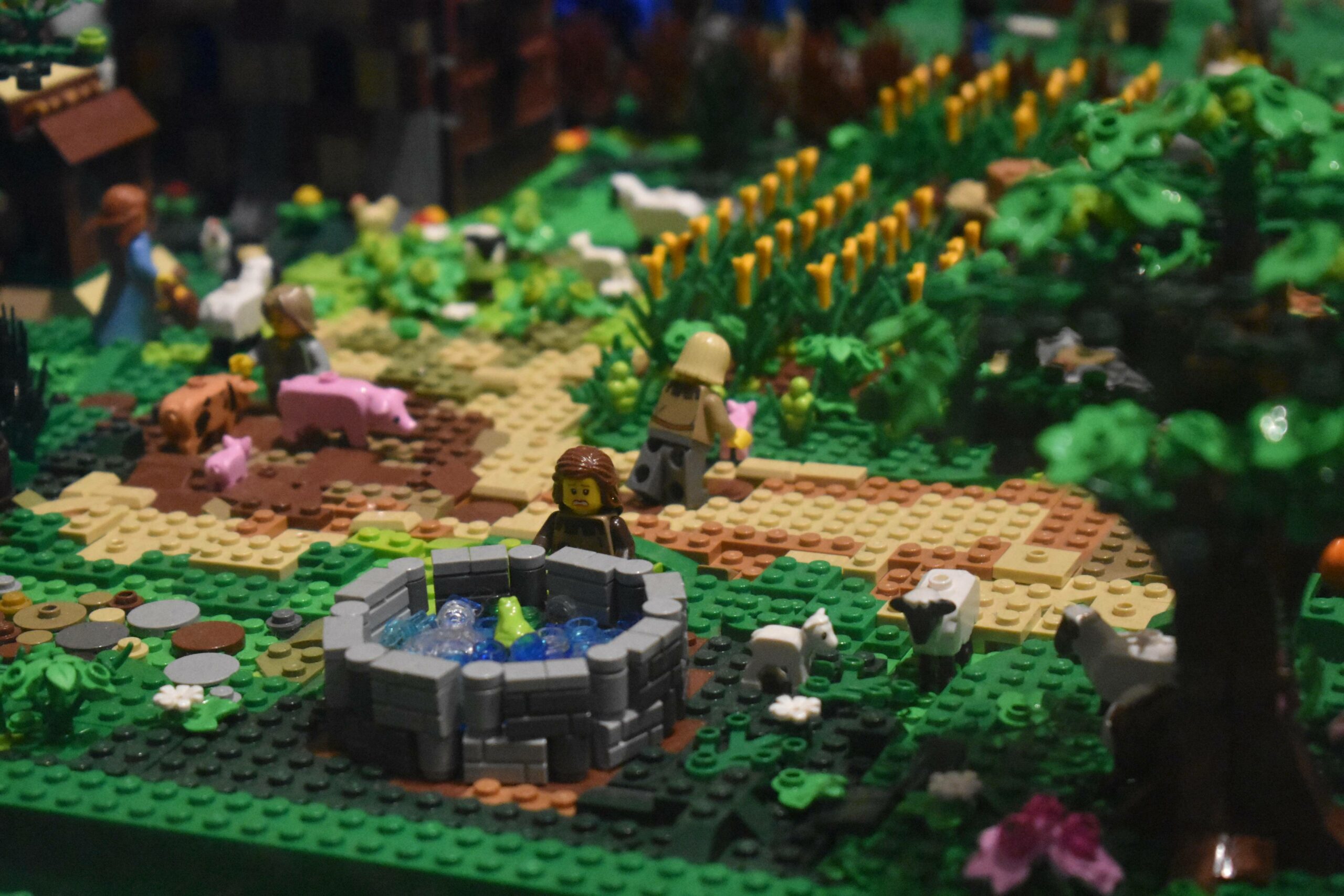 A photo of various lego people on a lego set that resembles a green field with lego animals like a sheep and pigs.