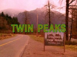 A hazy photo of a road surrounded by wilderness and mountain leading around a curve and a sign that says “welcome to twin peaks.”