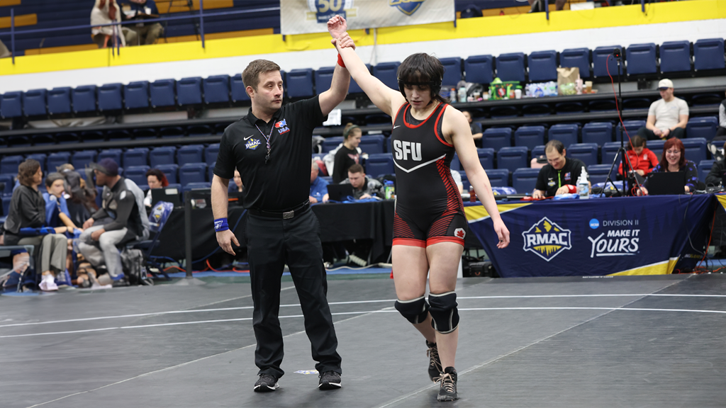 Wrestler on the SFU women’s team having their hand raised after beating their opponent.