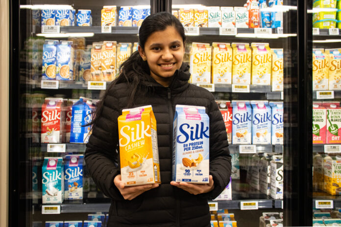 Person standing in the dairy alternative aisle at grocery store holding almond and cashew milk.