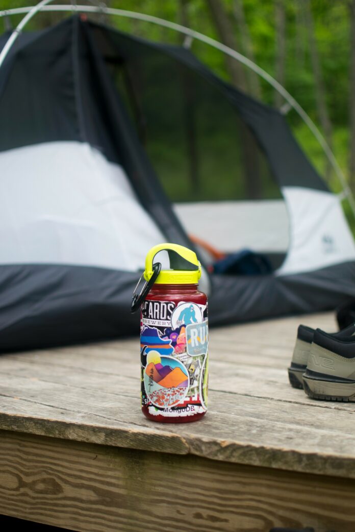 A red water bottle covered in stickers on a table next to a tent.