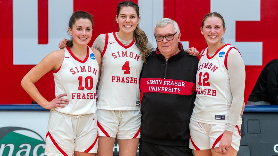 Photo of SFU women’s head coach posing with three of his players on the sideline.