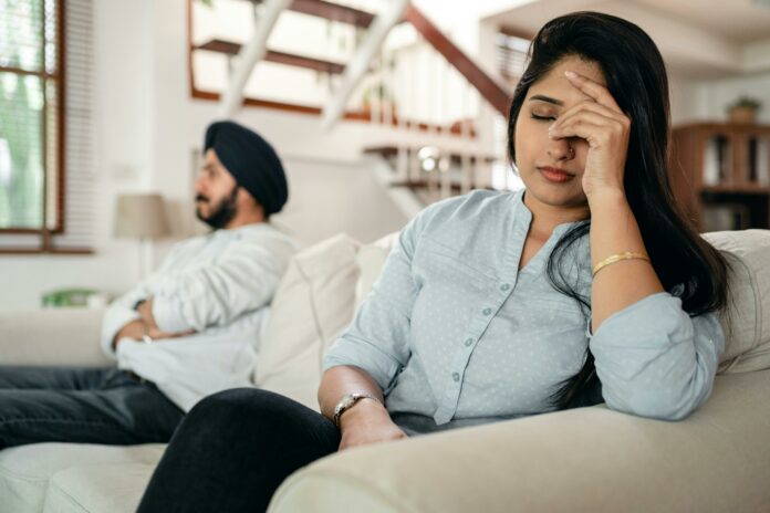 Connections Upset couple sitting on a couch. He has his arms crossed and she has her hand on her face looking exasperated.