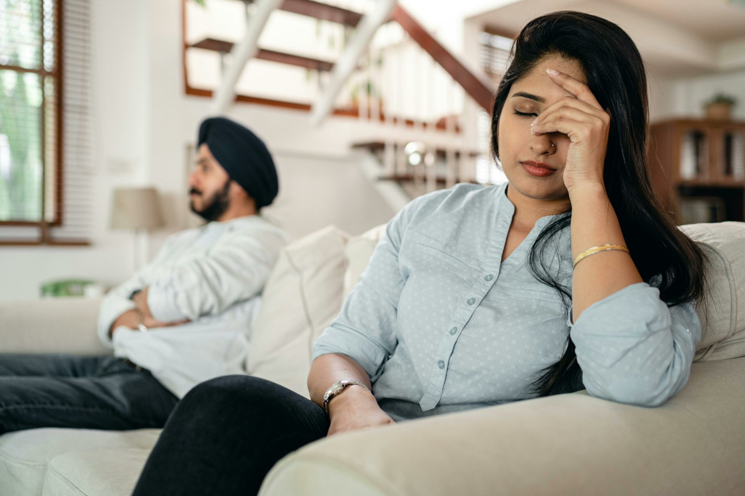 Upset couple sitting on a couch. He has his arms crossed and she has her hand on her face looking exasperated.