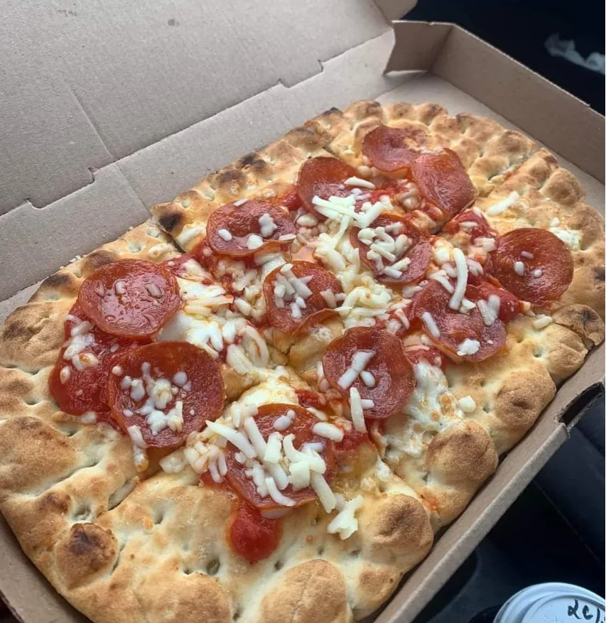 Photo of a box with an ovular flatbread inside. On top are pepperoni and a small amount of unmelted cheese