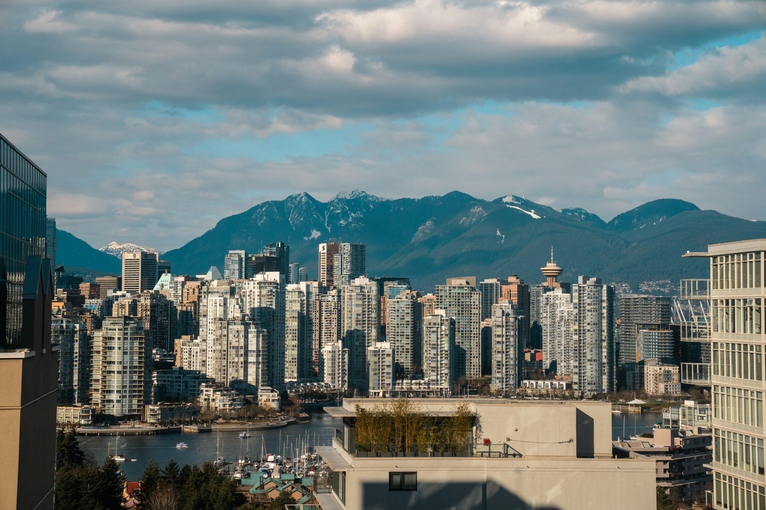 Vancouver skyline in afternoon light with the Burrard Inlet and skyscrapers in the foreground. In the background are the North Shore mountains with a dusting of snow.