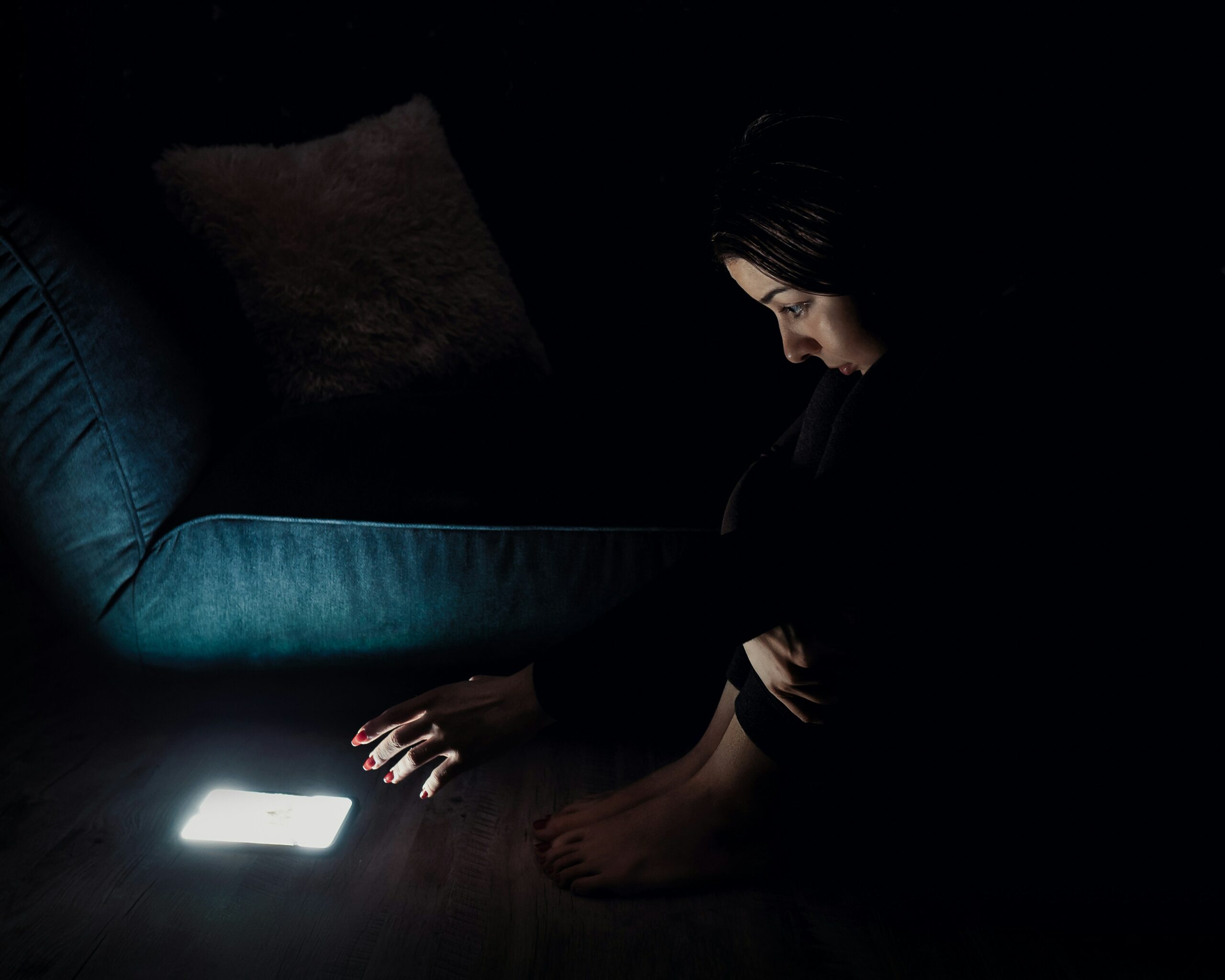 Woman sitting in a dark room. Her face is illuminated by the light coming from her phone.