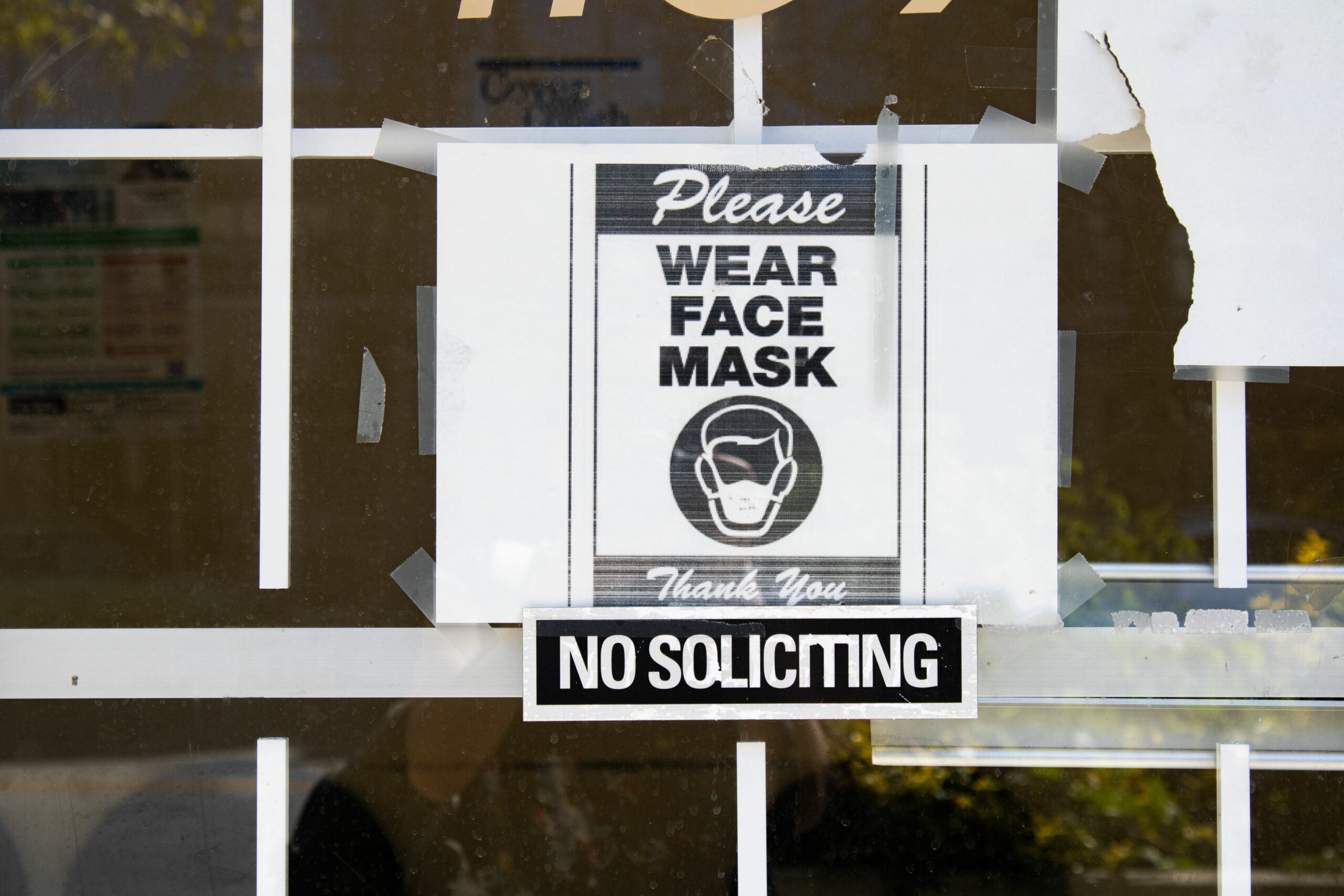 A window displaying a sign that says “wear a face mask.”