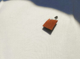 a close-up of a tan moose hide pin on a white shirt