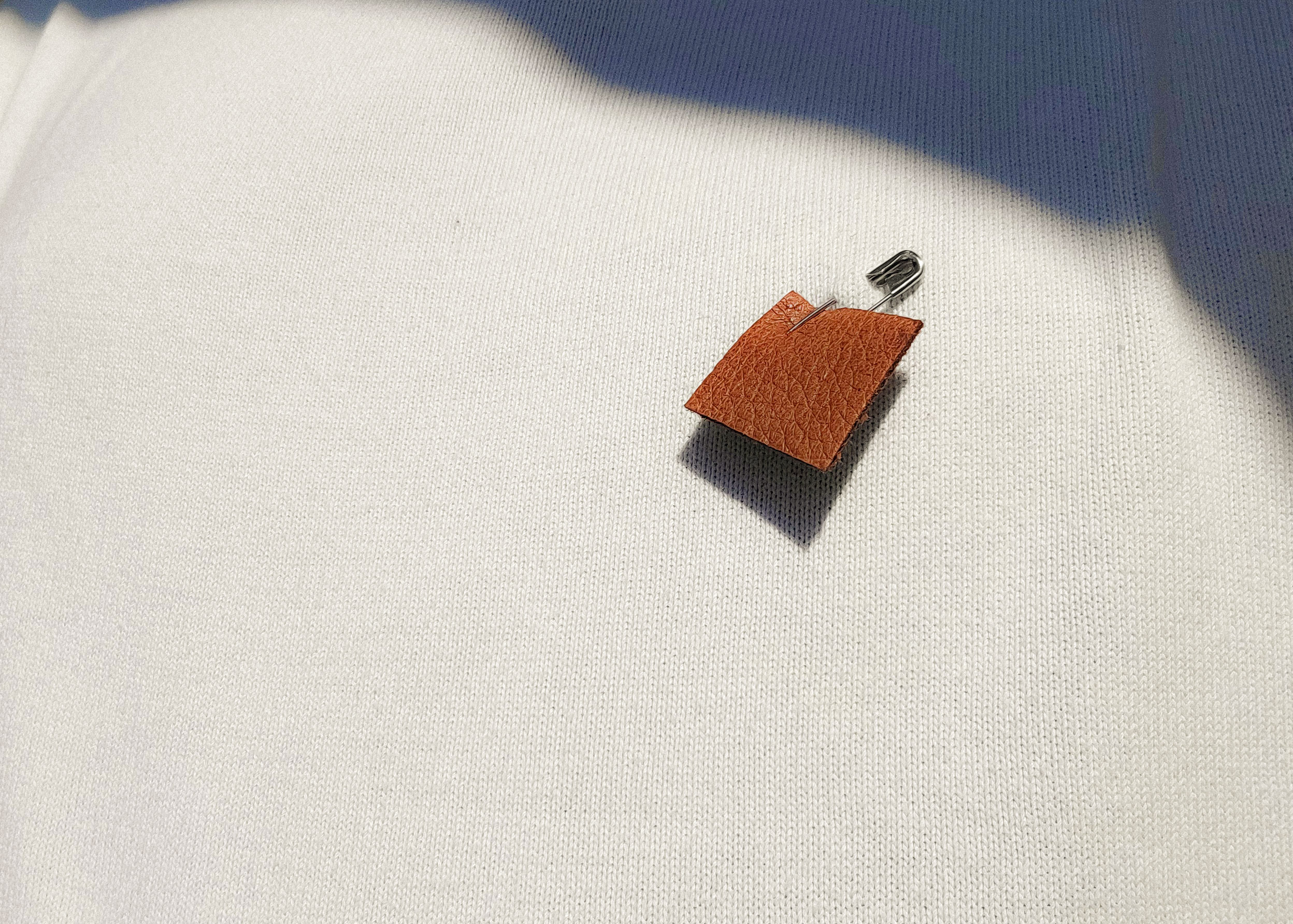 a close-up of a tan moose hide pin on a white shirt