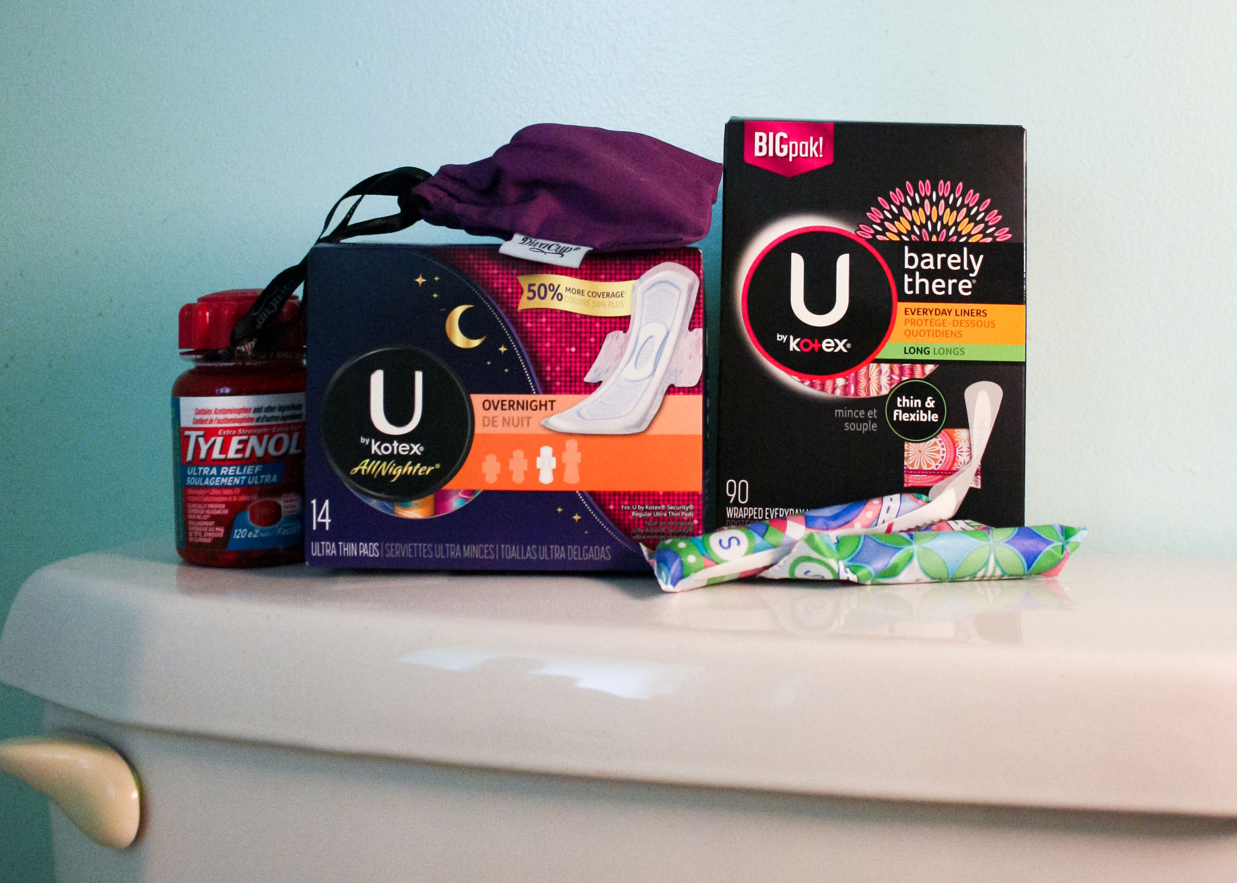 various period products, pads, and tampons stacked on a toilet lid